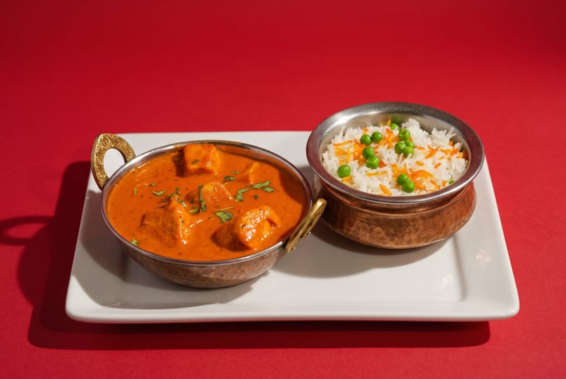 Paneer butter masala in a copper bowl with basmati rice and peas on a white plate.